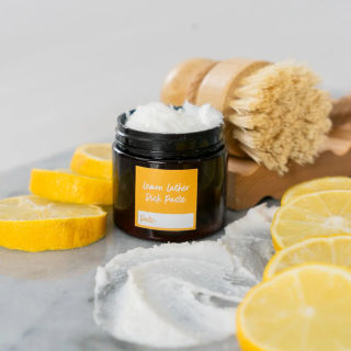 An amber jar of homemade lemon dish paste with lemon slices and a scrub brush