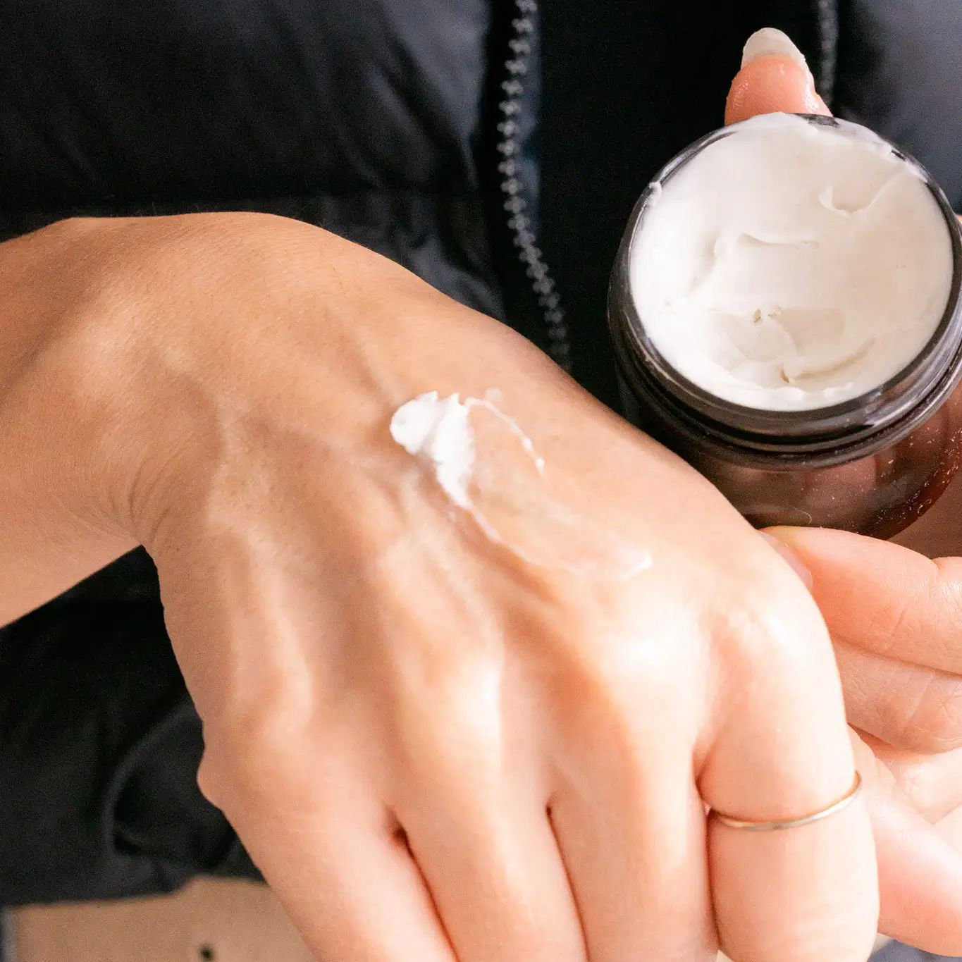Homemade body butter smoothed onto the back of a hand, beside its jar
