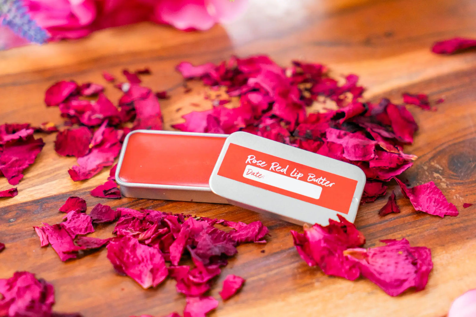 An open tin of homemade rose lip butter on scattered rose petals